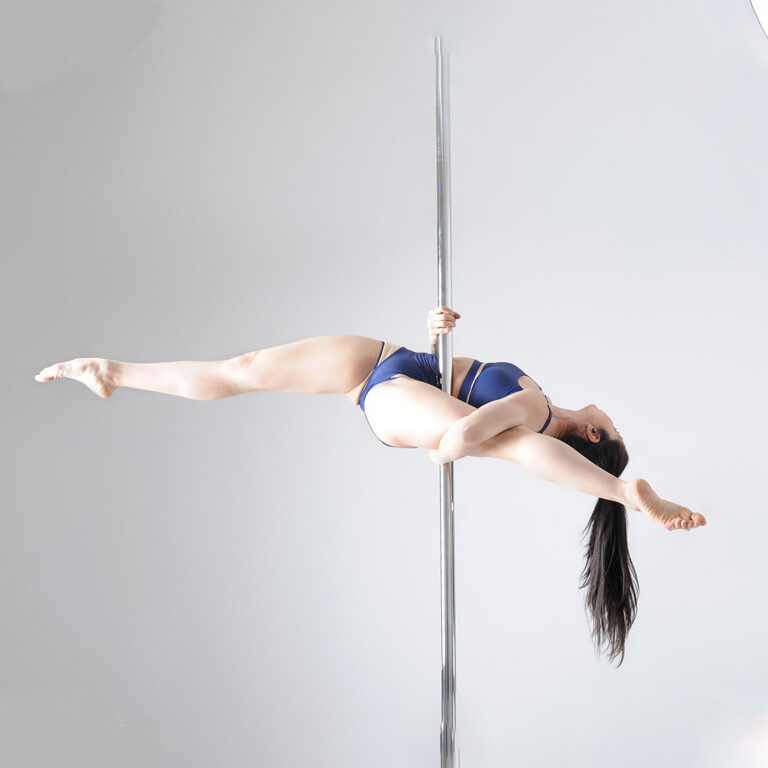 female pole dancing teacher performing advanced pole level 3-4 dance move in class at london dance academy
