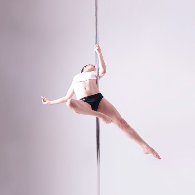 male pole dancing teacher performing spinning pole move in class at london dance academy
